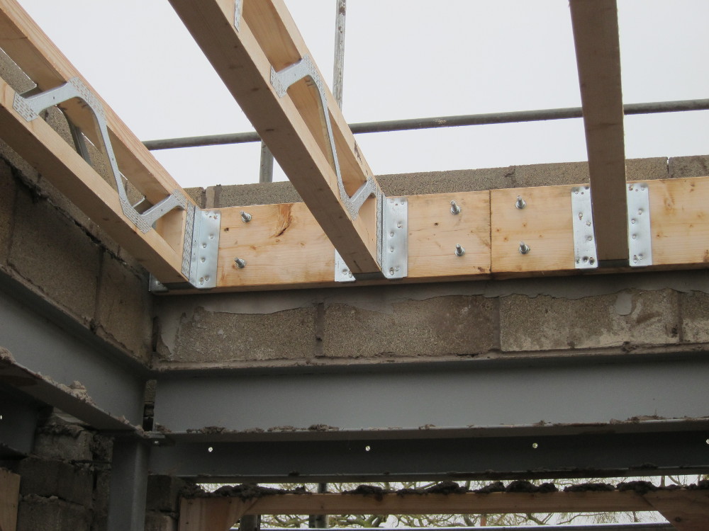 Joists installed on galvanized steel joist hangers on wall plate - note parge coat on blockwork